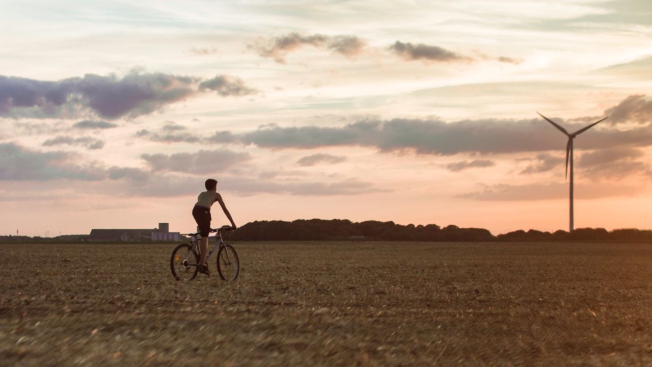 Niño en bicicleta en un campo con molinos de viento. PEXELS/HASAN ZAHRA