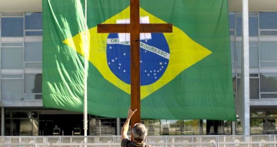 Un hombre con una cruz reza frente a bandera de Brasil, en el Palacio do Planalto de Brasilia. EFE/JOEDSON ALVES