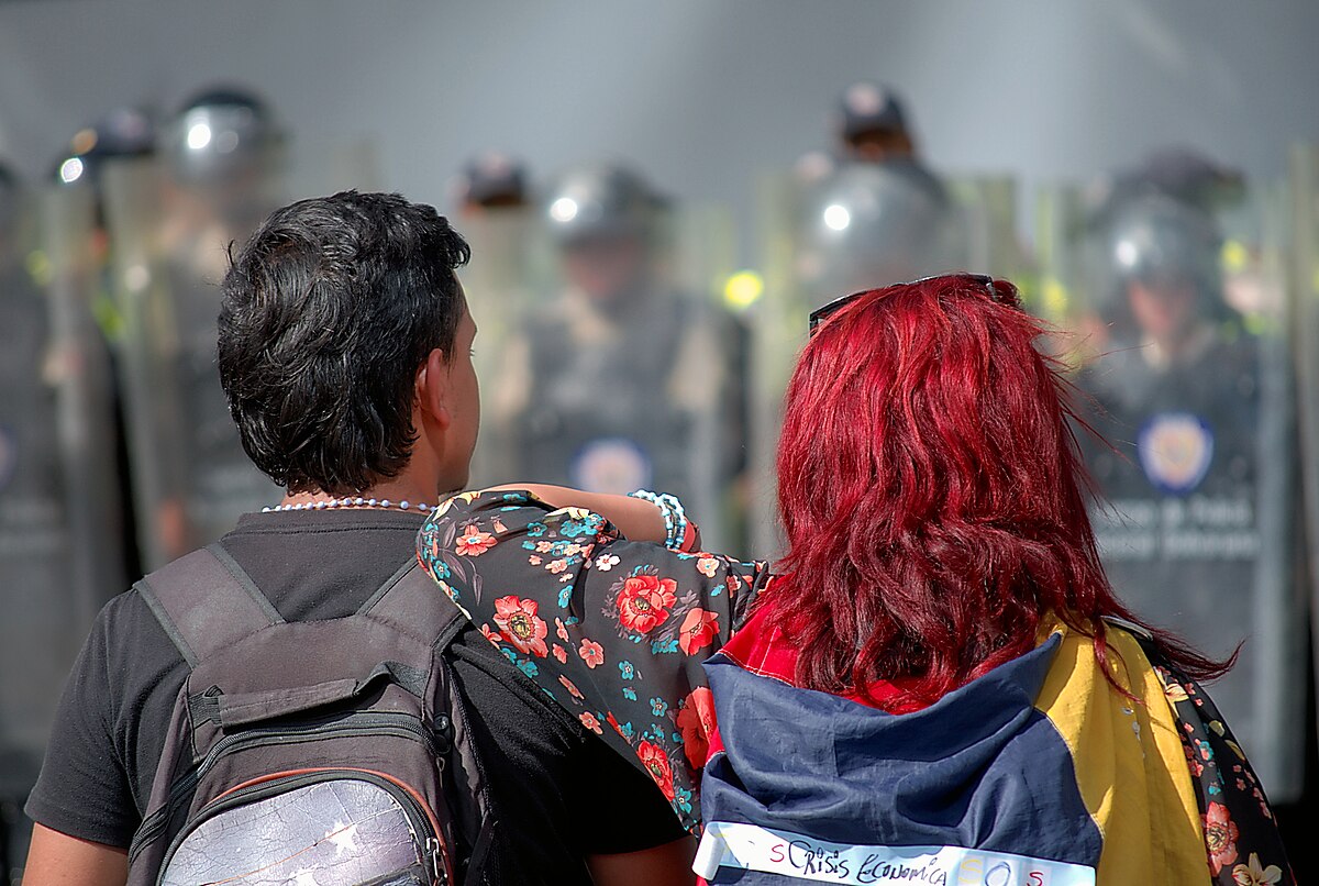 Dos venezolanos frente a la policía en Caracas, en un país donde la represión y la crisis han alimentado una diáspora que supera ya los nueve millones de migrantes. CARLOS DÍAZ