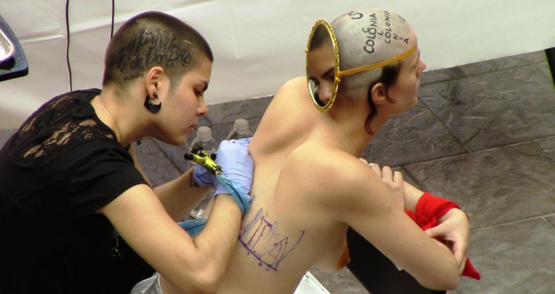 Lidiette del Valle tatuando la espalda de la artista Marina Barsy Janer, en 2014, durante la performance '(De) Colonial Reconquista' (2014), en el Museo de Arte Contemporáneo de Puerto Rico. CORTESÍA BARSY JANER/ARNALDO RODRÍGUEZ BAGUÉ
