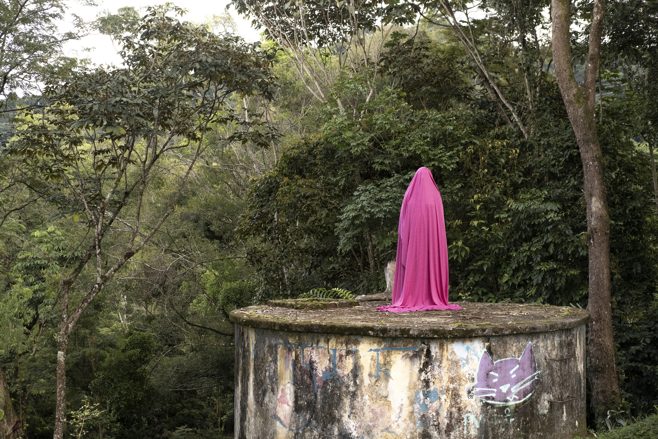 Una figura cubierta por una tela fucsia se alza sobre una estructura abandonada en medio de las montañas de Villavicencio, Meta, representando la diversidad de los cuerpos en medio de la naturaleza. MTQ Una figura cubierta por una tela fucsia se alza sobre una estructura abandonada en medio de las montañas de Villavicencio, Meta, representando la diversidad de los cuerpos en medio de la naturaleza. MTQ
